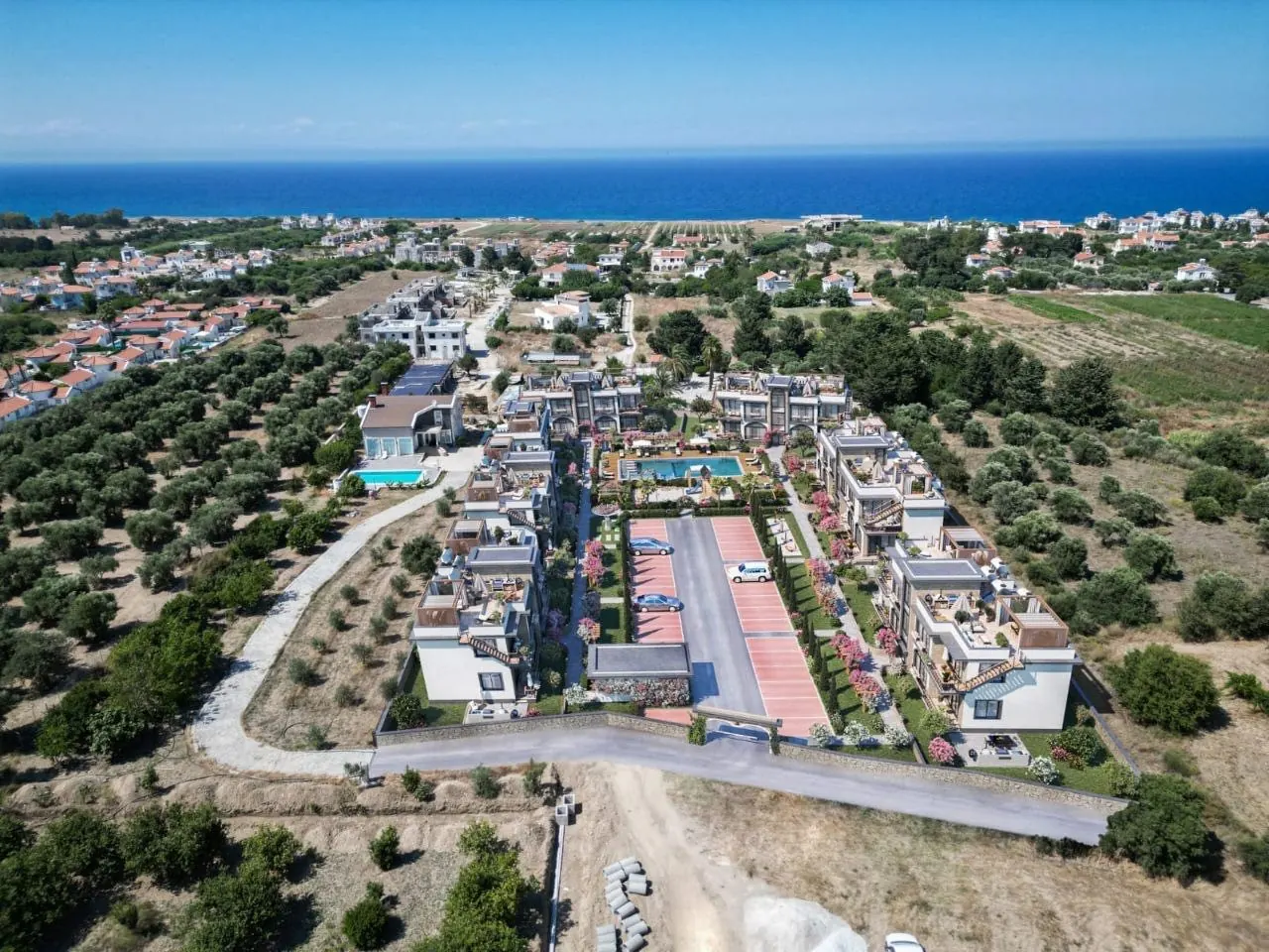 Aerial photograph of the Floral Homes site in Lapta with the blocks arranged around the pool and car park, olive groves either side and the sea beyond